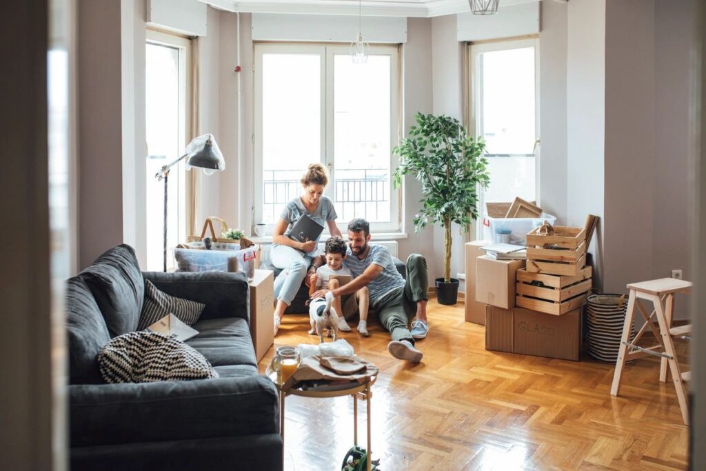 A young family sitting on the floor of their new home, petting a cat, moving boxes beside them